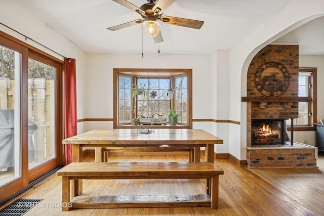 dining area with ceiling fan, a fireplace, light hardwood / wood-style floors, and a healthy amount of sunlight