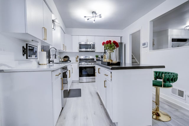 kitchen featuring appliances with stainless steel finishes, white cabinets, light wood-type flooring, sink, and a breakfast bar area