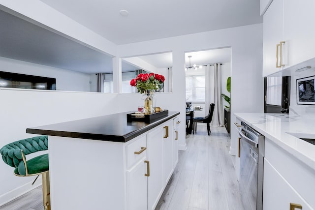 kitchen featuring white cabinets, light wood-type flooring, a kitchen island, and stainless steel dishwasher