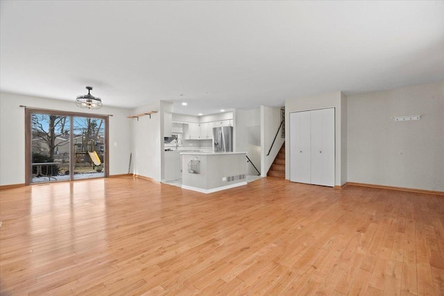 unfurnished living room featuring light wood-type flooring and an inviting chandelier