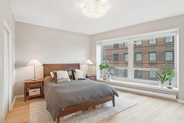 bedroom with an inviting chandelier, light hardwood / wood-style flooring, and a baseboard radiator