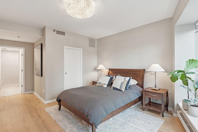 bedroom with a notable chandelier, ensuite bath, and light hardwood / wood-style flooring