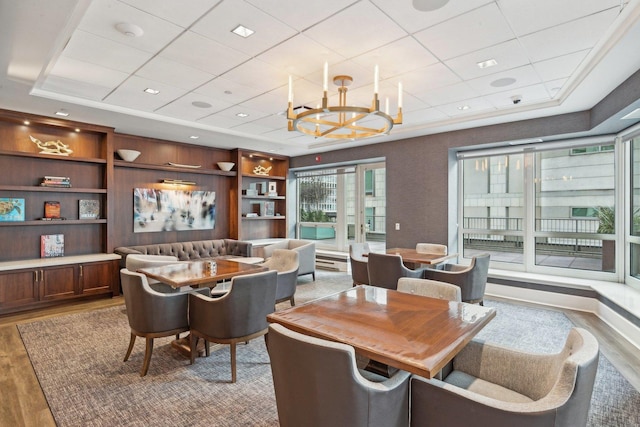 dining space featuring an inviting chandelier, built in shelves, wood-type flooring, and a tray ceiling