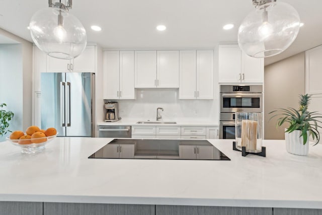 kitchen featuring sink, appliances with stainless steel finishes, white cabinetry, tasteful backsplash, and decorative light fixtures