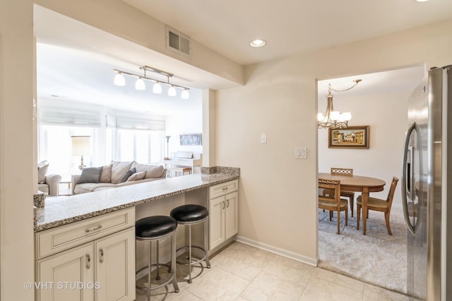 kitchen featuring stainless steel refrigerator, a kitchen breakfast bar, light stone counters, cream cabinets, and a chandelier