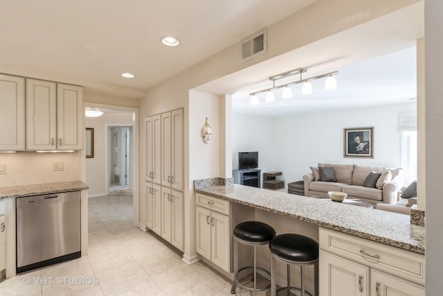 kitchen featuring a breakfast bar, dishwasher, light stone countertops, cream cabinets, and backsplash