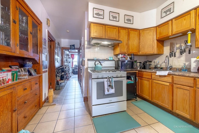 kitchen with light tile patterned floors, white gas range oven, decorative backsplash, brown cabinets, and a sink