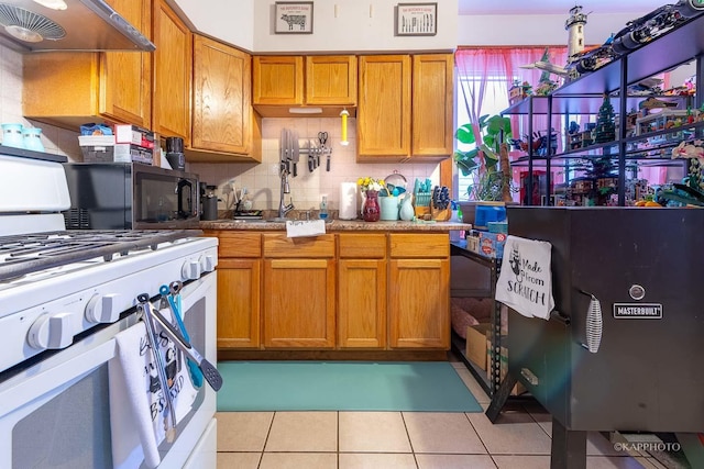 kitchen featuring brown cabinetry, white range with gas cooktop, under cabinet range hood, and light tile patterned floors