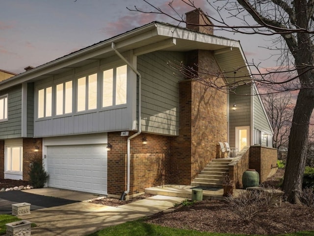 exterior space with a garage, concrete driveway, brick siding, and a chimney