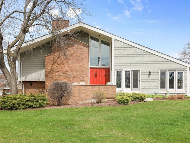 back of house with a yard, brick siding, and a chimney