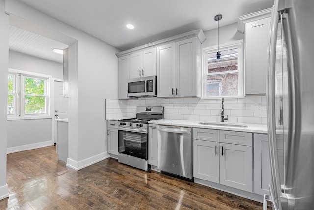 kitchen featuring decorative light fixtures, dark hardwood / wood-style flooring, stainless steel appliances, sink, and backsplash