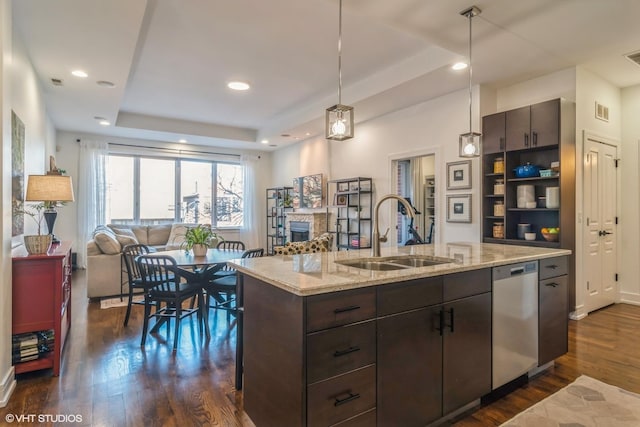 kitchen with dark wood-type flooring, sink, dishwasher, a raised ceiling, and a kitchen island with sink