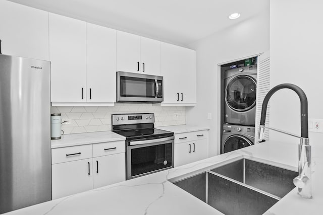 kitchen with light stone counters, appliances with stainless steel finishes, stacked washing maching and dryer, and white cabinets