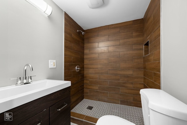 bathroom with toilet, tiled shower, and vanity