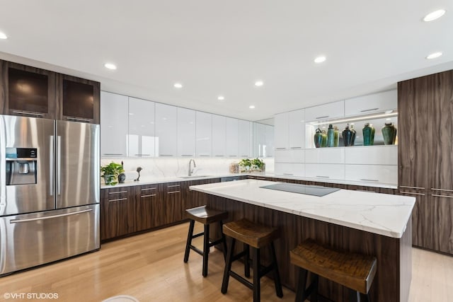 kitchen with sink, a breakfast bar, stainless steel refrigerator with ice dispenser, black electric stovetop, and a kitchen island