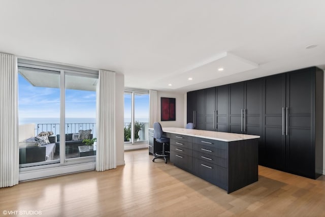 kitchen with light wood-type flooring, a kitchen island, floor to ceiling windows, and a water view