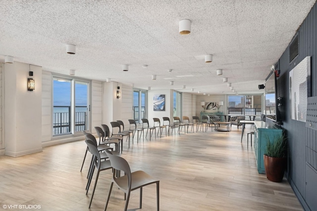 dining room featuring expansive windows, a water view, a healthy amount of sunlight, and light wood-type flooring