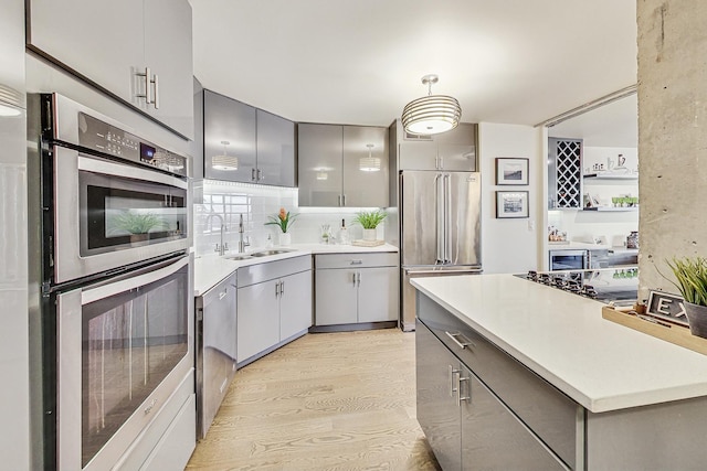 kitchen with pendant lighting, sink, gray cabinetry, stainless steel appliances, and light hardwood / wood-style flooring