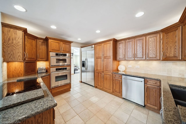 kitchen featuring appliances with stainless steel finishes, dark stone counters, brown cabinets, and tasteful backsplash