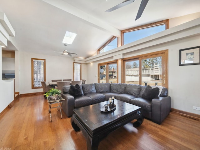 living room featuring a ceiling fan, lofted ceiling with skylight, visible vents, and light wood-style floors