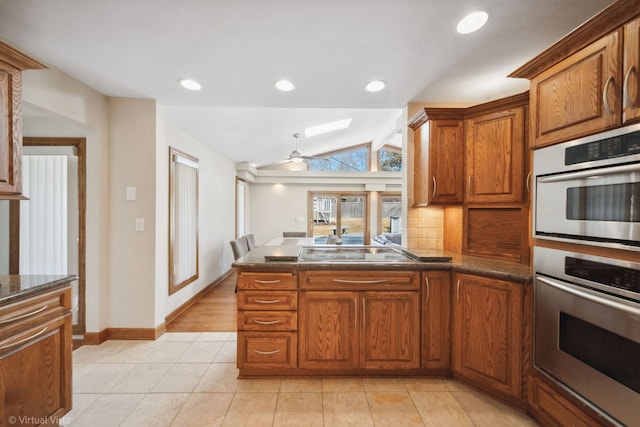 kitchen with double oven, black electric stovetop, brown cabinetry, and vaulted ceiling with skylight