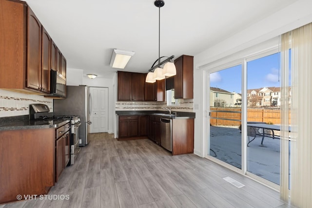 kitchen with hanging light fixtures, decorative backsplash, light hardwood / wood-style flooring, and stainless steel appliances