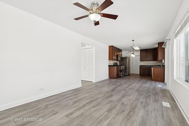 unfurnished living room featuring ceiling fan, light hardwood / wood-style floors, sink, and a healthy amount of sunlight