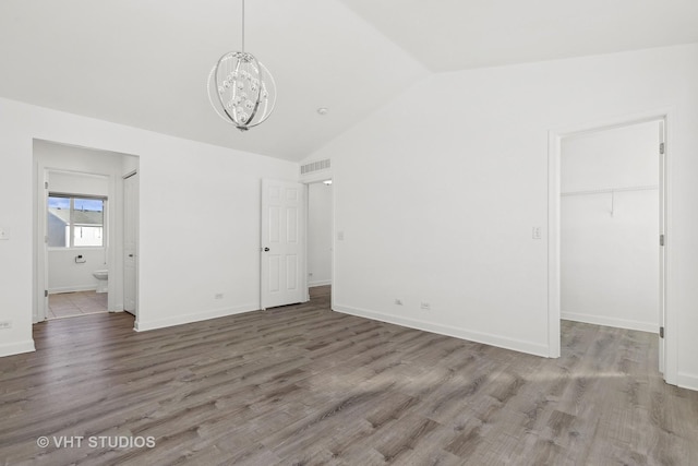 unfurnished bedroom with lofted ceiling, a walk in closet, wood-type flooring, a chandelier, and a closet