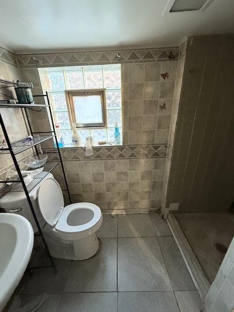 bathroom with tile patterned floors, tile walls, sink, tiled shower, and toilet