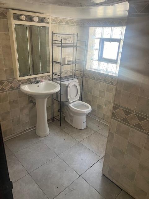 bathroom with toilet, tile patterned floors, and tile walls