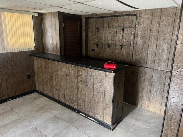 bar featuring a drop ceiling, wooden walls, and dark brown cabinets