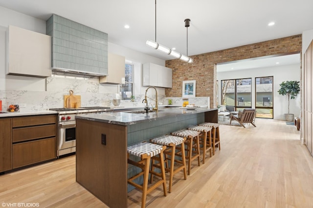 kitchen featuring white cabinets, dark stone counters, sink, high end stainless steel range oven, and a center island with sink