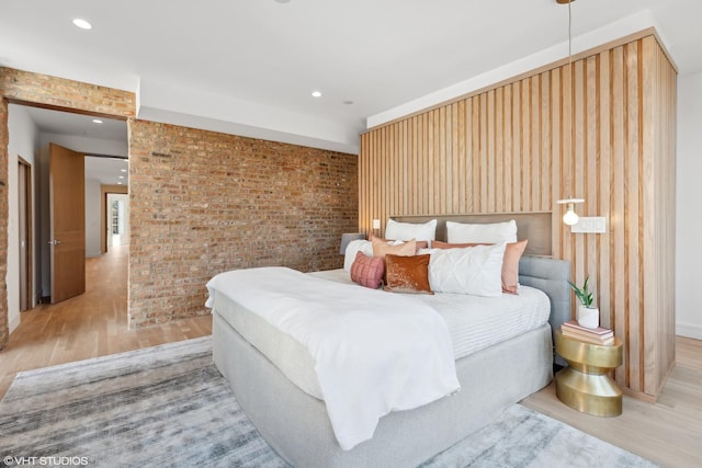 bedroom featuring brick wall and light hardwood / wood-style flooring