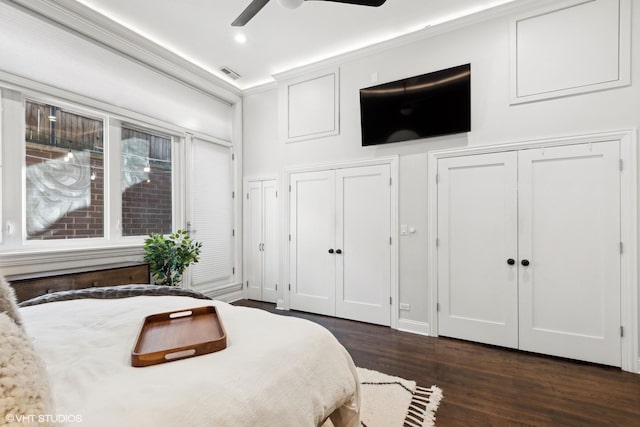 bedroom with crown molding, dark wood-type flooring, two closets, and ceiling fan