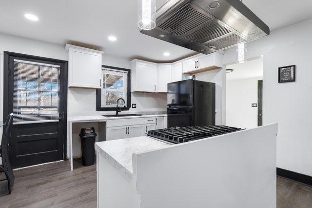 kitchen featuring black fridge, white cabinetry, range hood, and sink