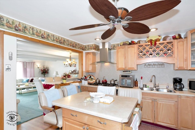 kitchen with light brown cabinetry, sink, wall chimney range hood, backsplash, and ceiling fan with notable chandelier