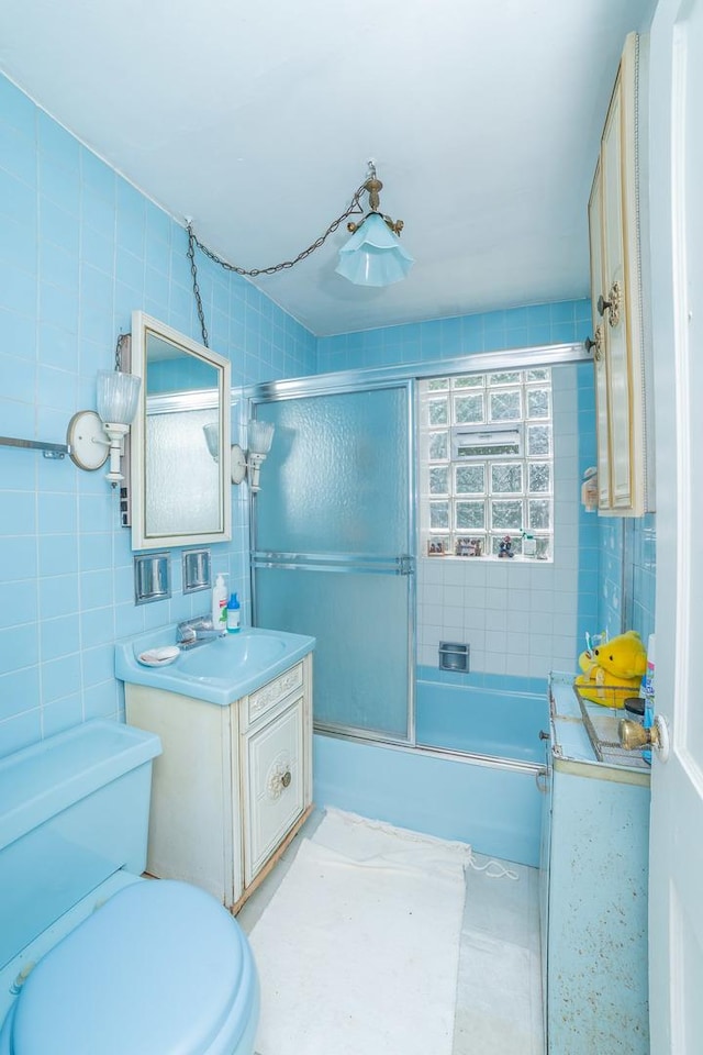 full bathroom featuring toilet, vanity, enclosed tub / shower combo, and tile walls