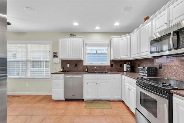 kitchen with light tile patterned floors, sink, appliances with stainless steel finishes, dark stone countertops, and white cabinets