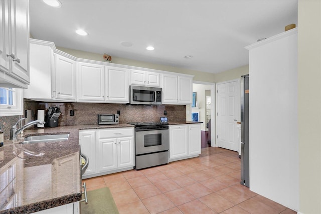 kitchen with appliances with stainless steel finishes, white cabinetry, sink, decorative backsplash, and light tile patterned floors