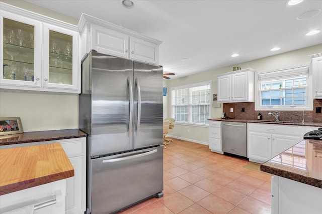 kitchen with light tile patterned flooring, sink, white cabinets, stainless steel appliances, and a healthy amount of sunlight