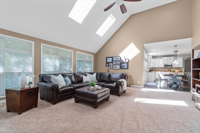 carpeted living room with a skylight, high vaulted ceiling, and ceiling fan