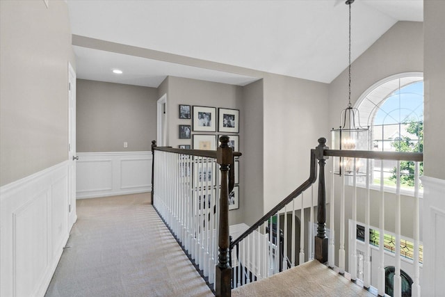 hallway with lofted ceiling, light carpet, and a chandelier