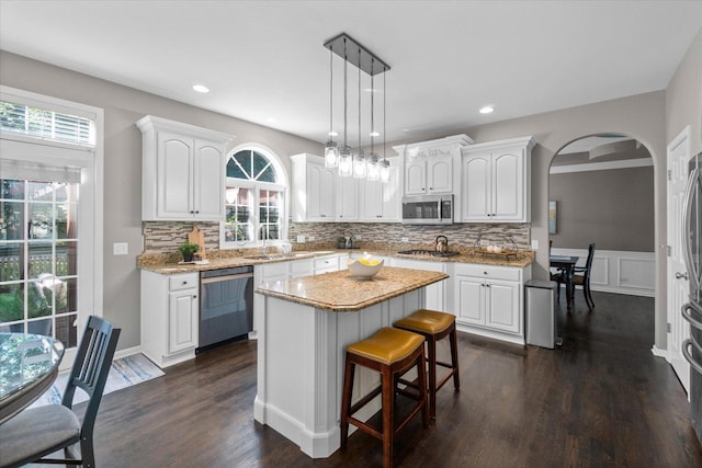 kitchen with dark wood-type flooring, stainless steel appliances, a center island, white cabinets, and decorative light fixtures