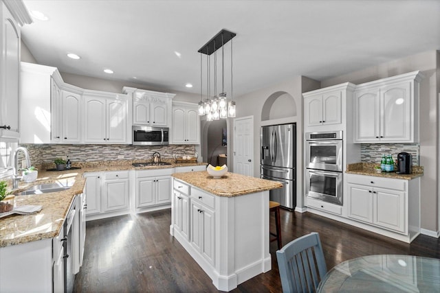 kitchen with a kitchen island, appliances with stainless steel finishes, white cabinetry, sink, and hanging light fixtures