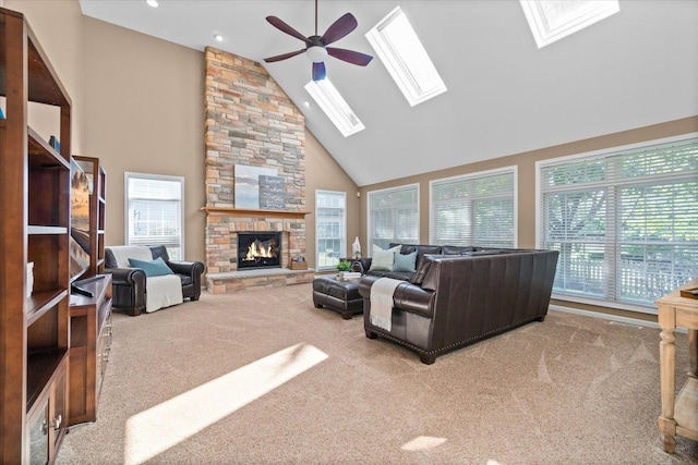 living room featuring a stone fireplace, light carpet, ceiling fan, and a skylight