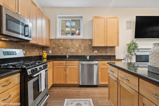 kitchen featuring sink, stainless steel appliances, light hardwood / wood-style floors, decorative backsplash, and dark stone counters