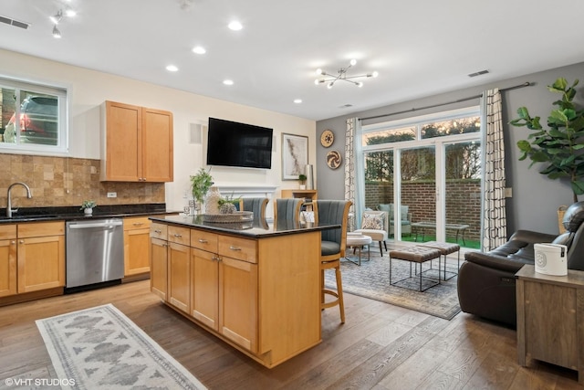 kitchen featuring sink, a kitchen island, a kitchen bar, stainless steel dishwasher, and light wood-type flooring