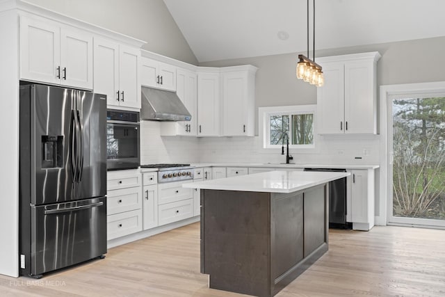 kitchen with hanging light fixtures, white cabinets, ventilation hood, light hardwood / wood-style floors, and stainless steel appliances