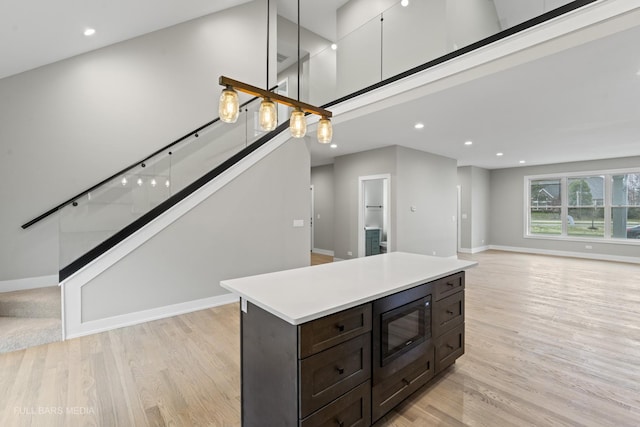 kitchen featuring a towering ceiling, decorative light fixtures, light hardwood / wood-style floors, dark brown cabinets, and built in microwave