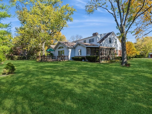 back of property with a lawn, a sunroom, and a wooden deck